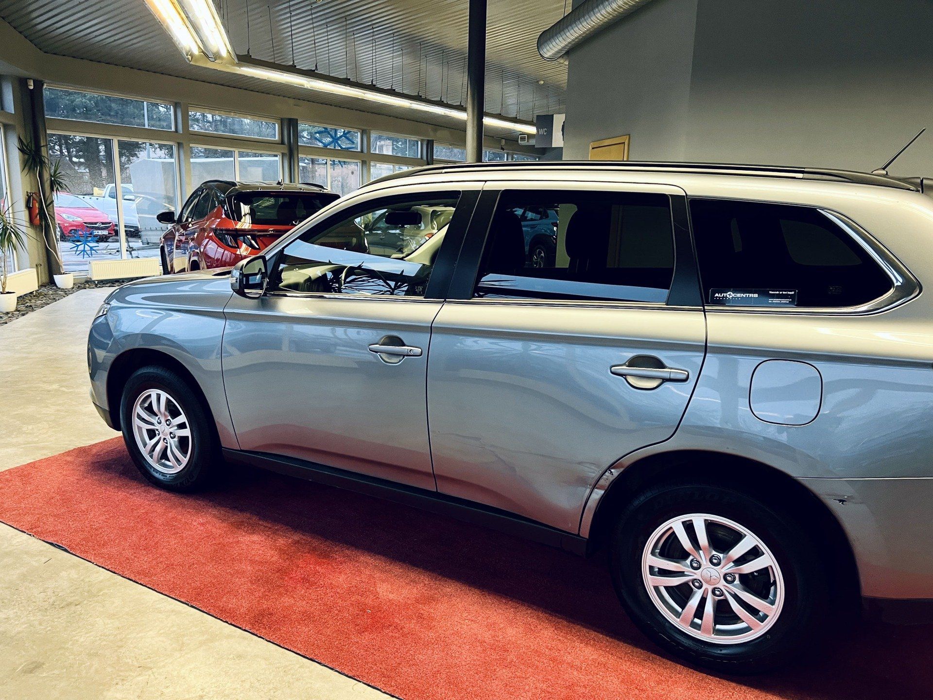 Sudraba automašīna ir novietota uz sarkanā paklāja izstāžu zālē.