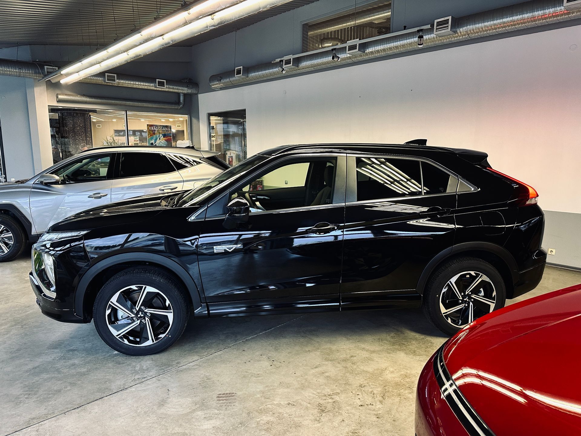 Melna automašīna ir novietota blakus sarkanai automašīnai salonā.