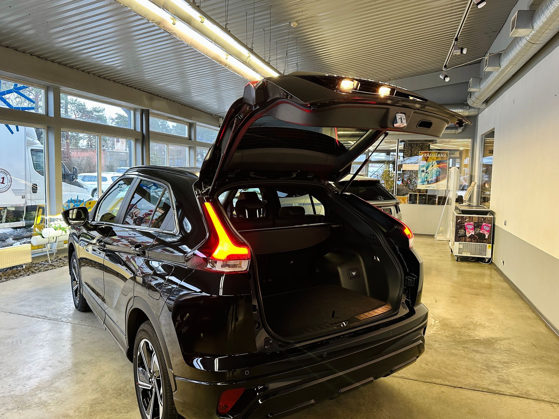 Melna automašīna ar atvērtu bagāžnieku ir novietota salonā.