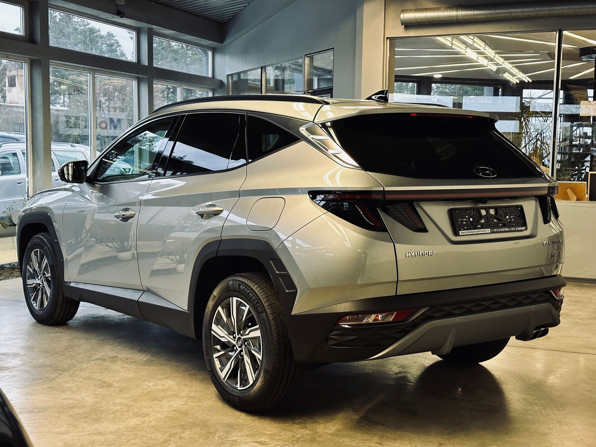 Sudraba auto stāv salonā ar daudz logiem.