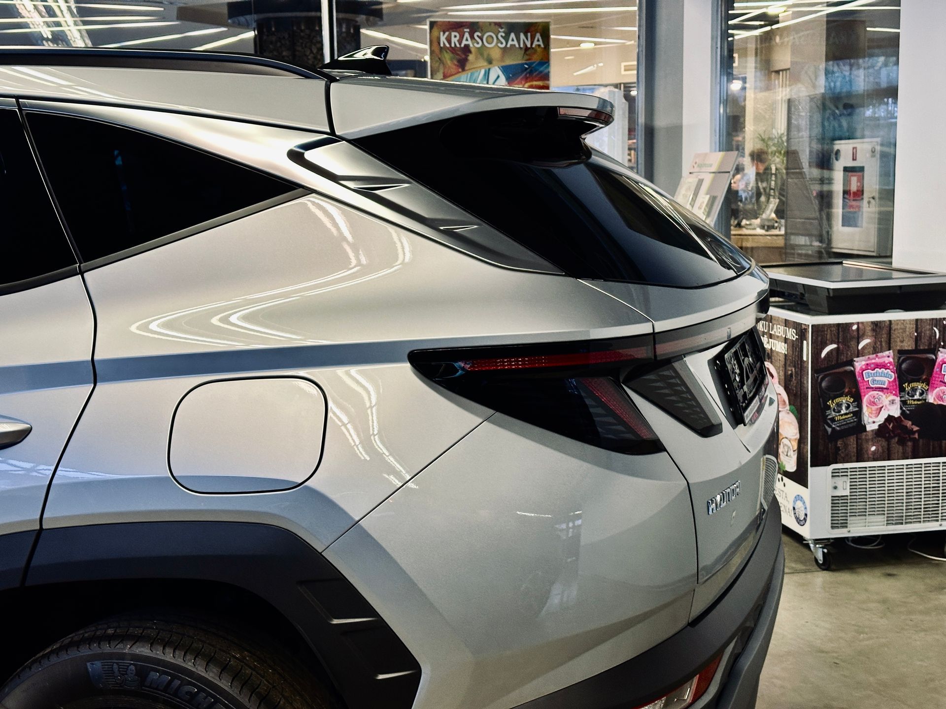 Sudraba auto stāv veikalā pie dzesētāja.