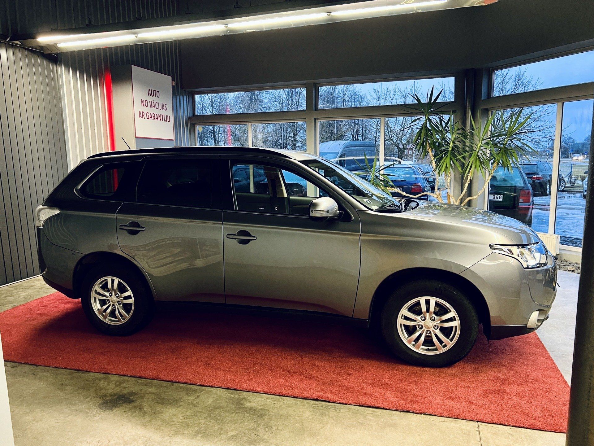 Sudraba automašīna sēž uz sarkana paklāja izstāžu zālē.