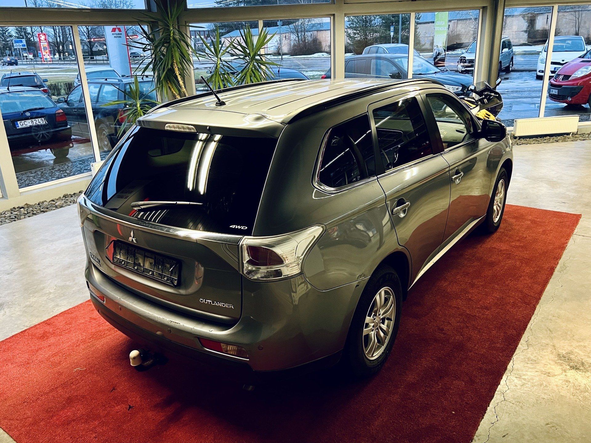 Pelēka automašīna ir novietota uz sarkana paklāja salonā.