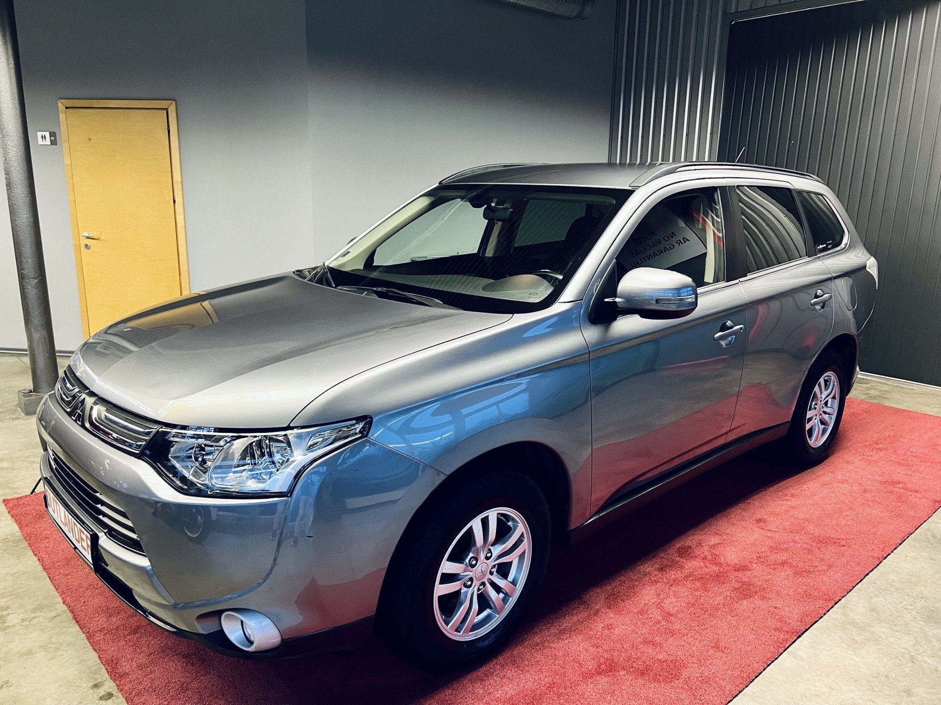 Sudraba auto stāv garāžā uz sarkanā paklāja.