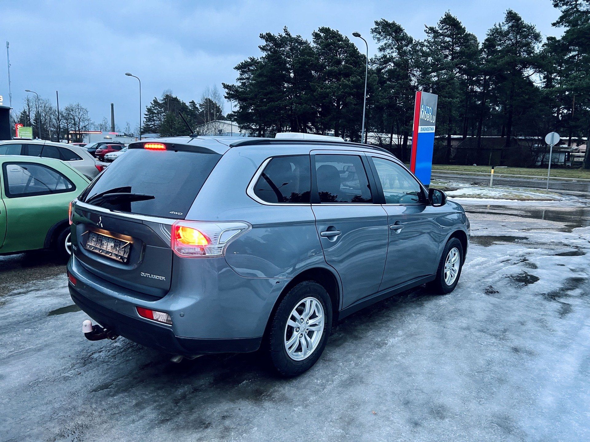 Pelēka mašīna stāv stāvvietā ar kokiem fonā.