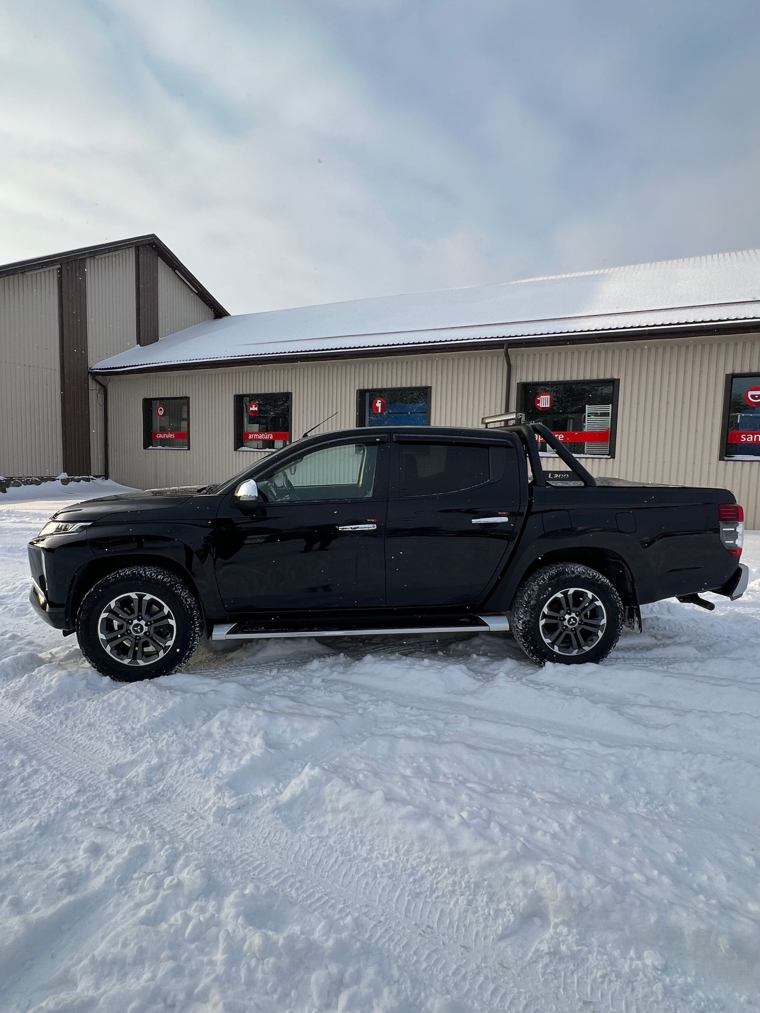 Melna kravas automašīna ir novietota sniegā pie ēkas.