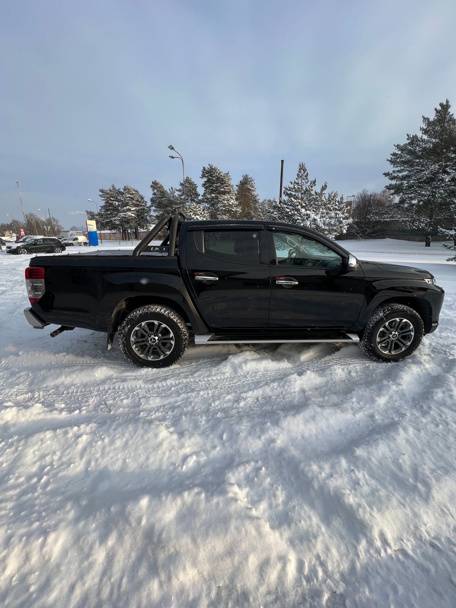 Melna kravas automašīna stāv sniegā stāvlaukumā.