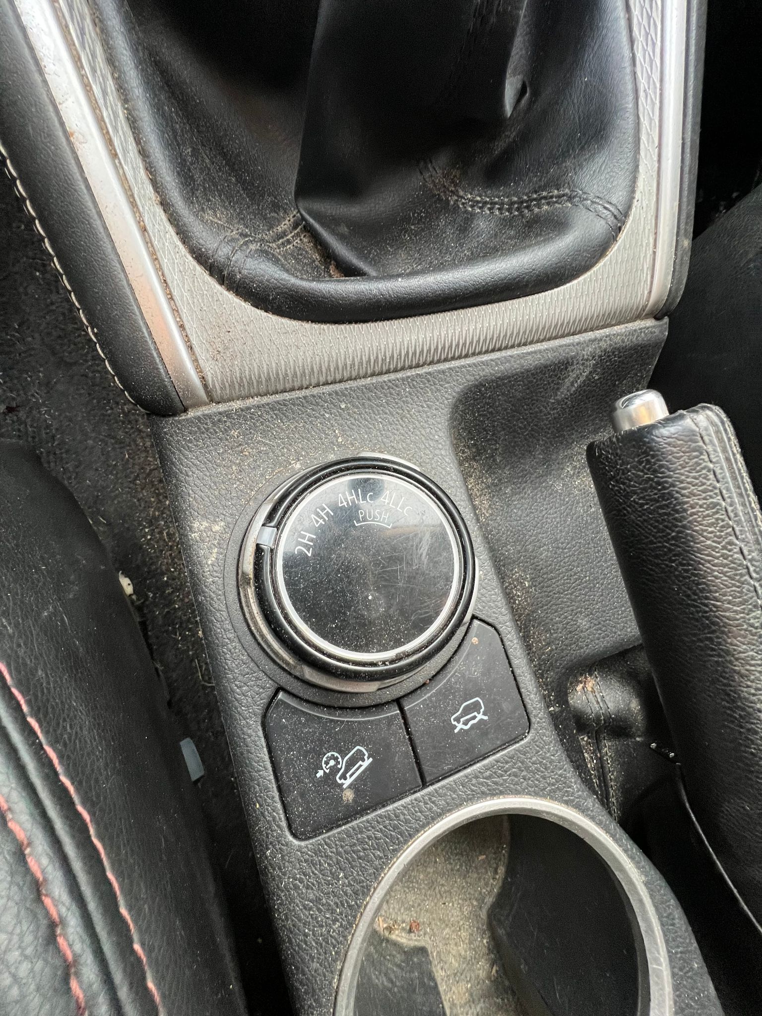 Netīra auto konsole ar glāžu turētāju un pārslēdzēju.