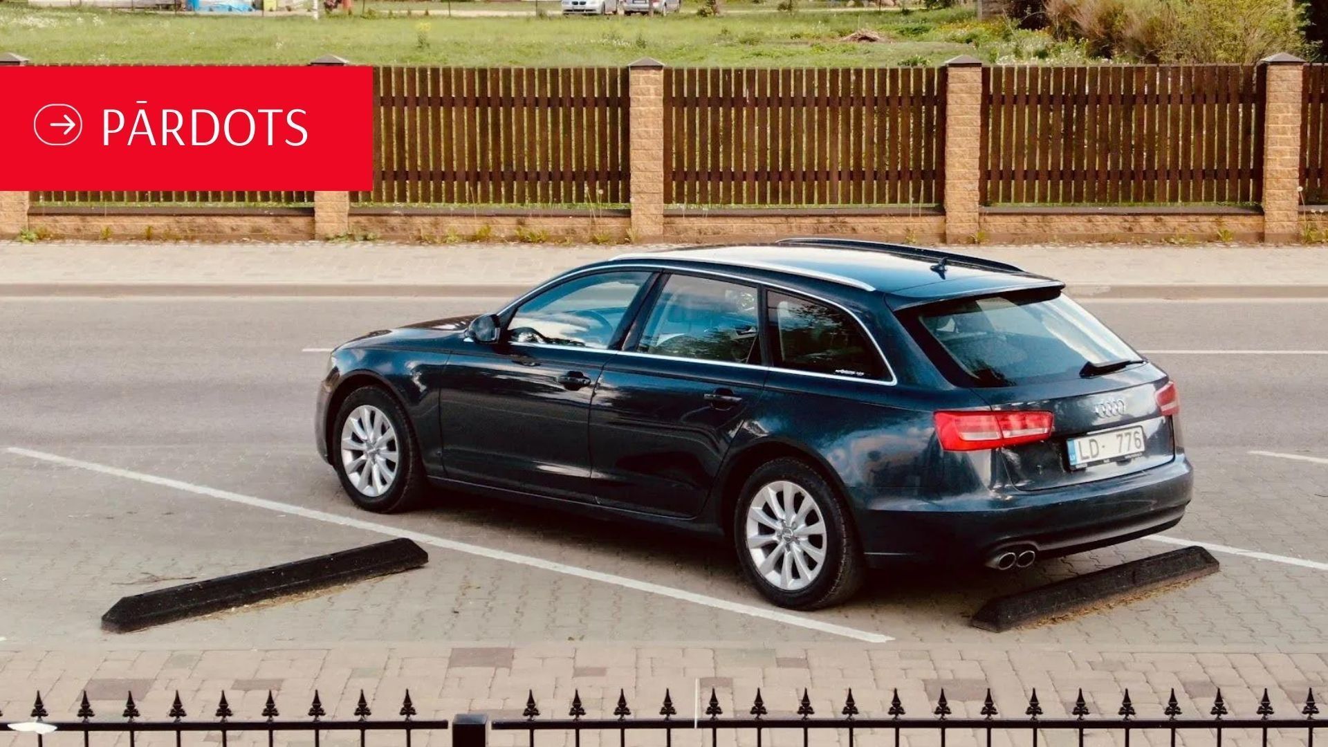 Melna mašīna stāv stāvvietā pie žoga.