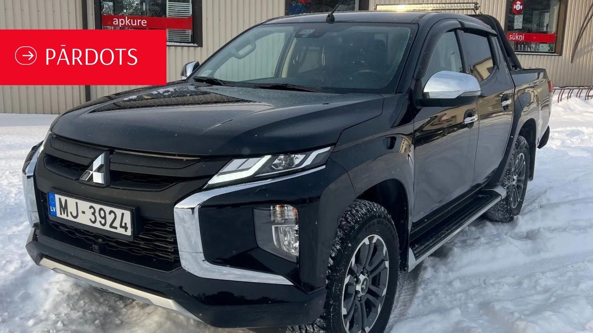 Melna kravas automašīna ir novietota sniegā pie ēkas.