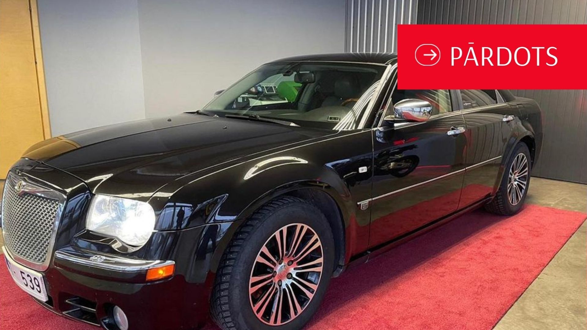 Melna mašīna stāv garāžā uz sarkana paklāja.