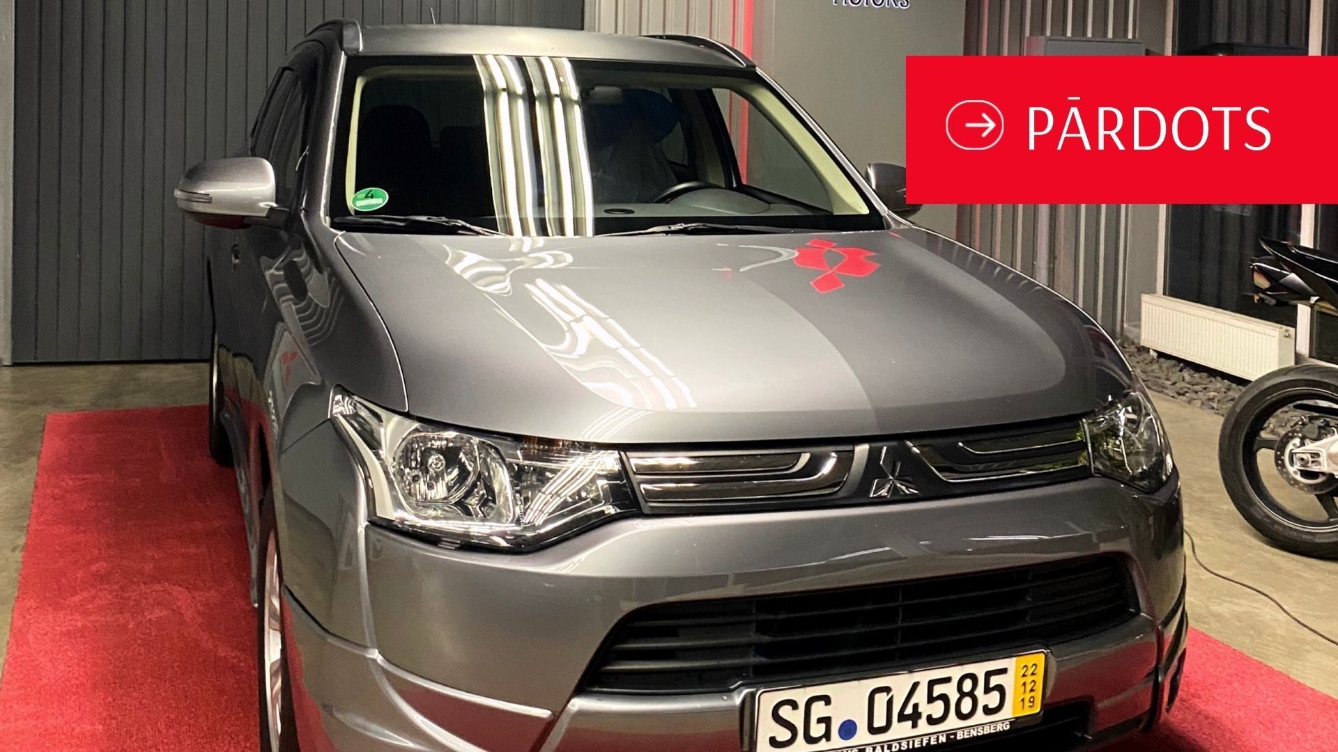 Pelēka mašīna stāv garāžā pie motocikla.