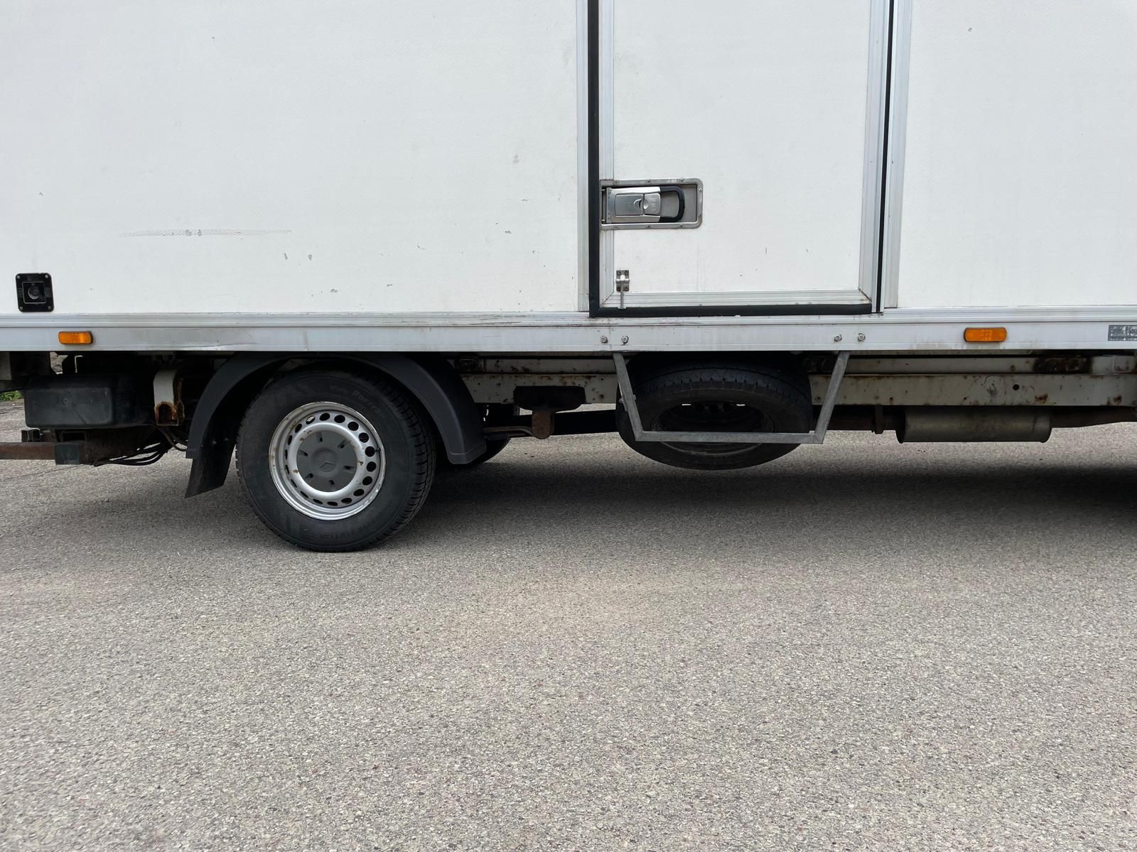 Ceļa malā stāv balta kravas automašīna.