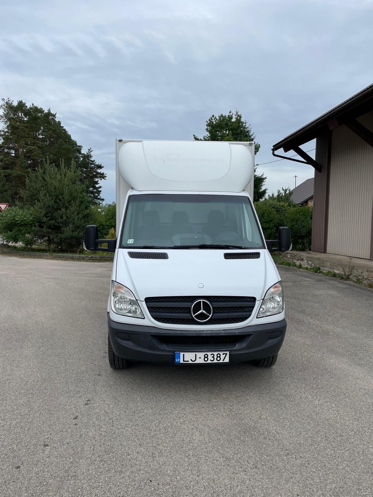 Autostāvvietā stāv balts mercedes furgons.