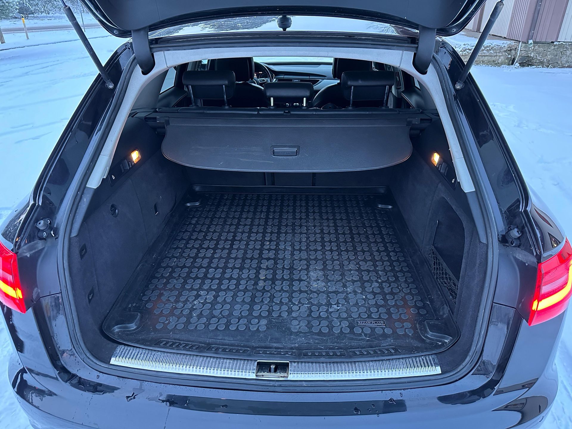Melnas mašīnas aizmugurē ar atvērtu bagāžnieku sēž sniegā.