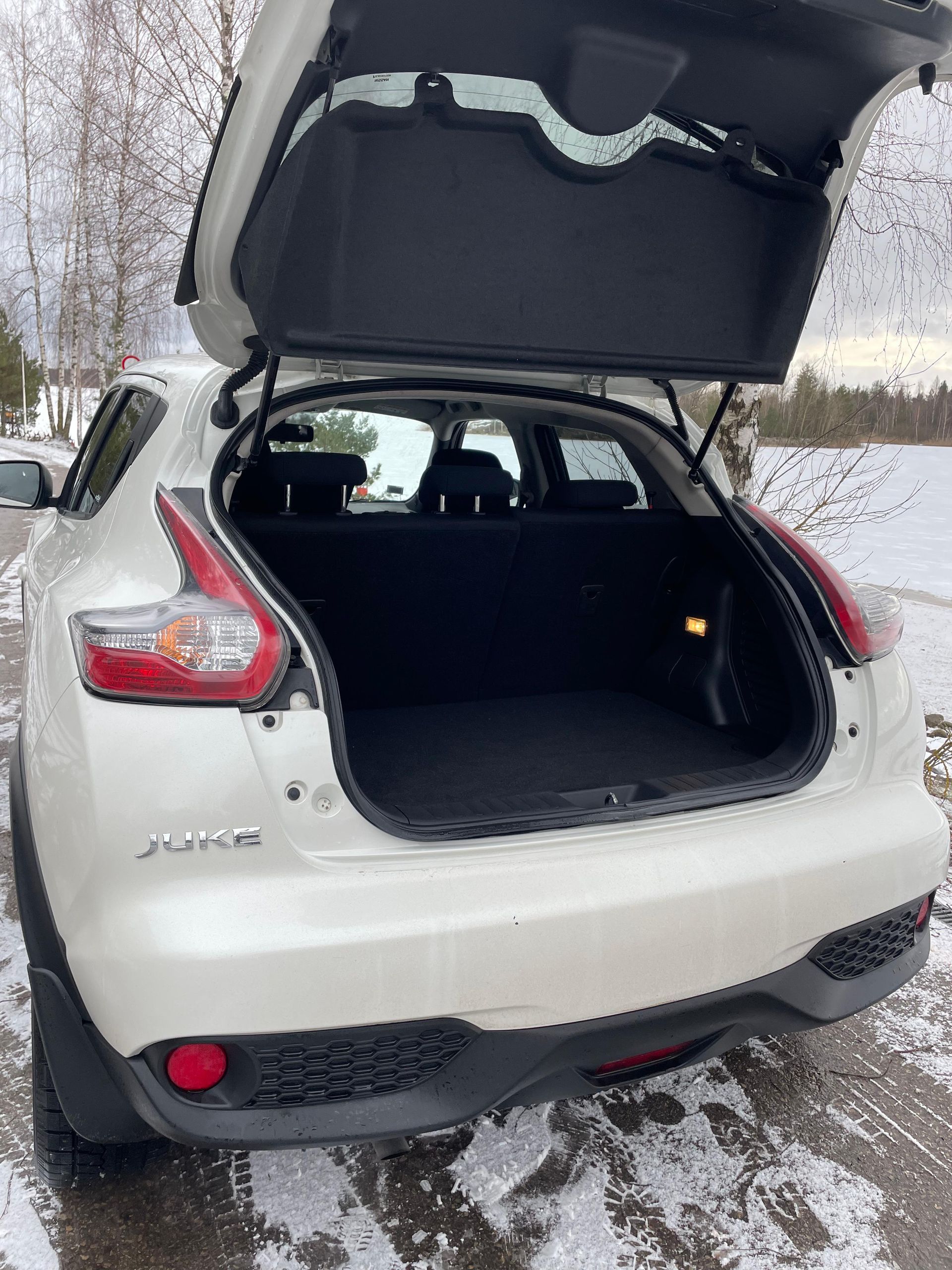 Sniegā stāv balts nissan juke ar atvērtu bagāžnieku.