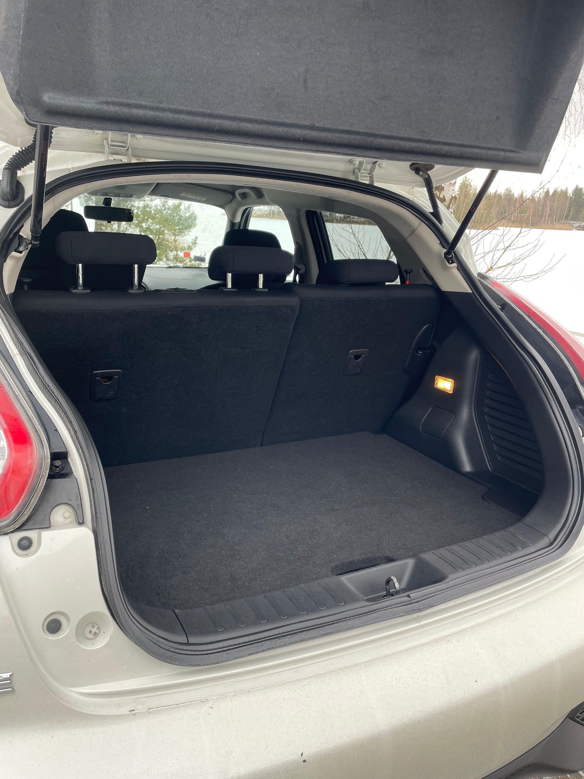 Baltas automašīnas aizmugure ar atvērtu bagāžnieku.