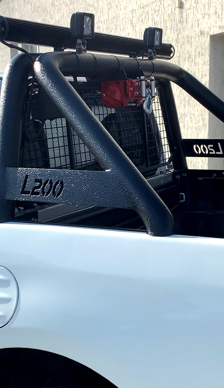 Balta kravas automašīna ar melnu joslu aizmugurē ir novietota pie ēkas.