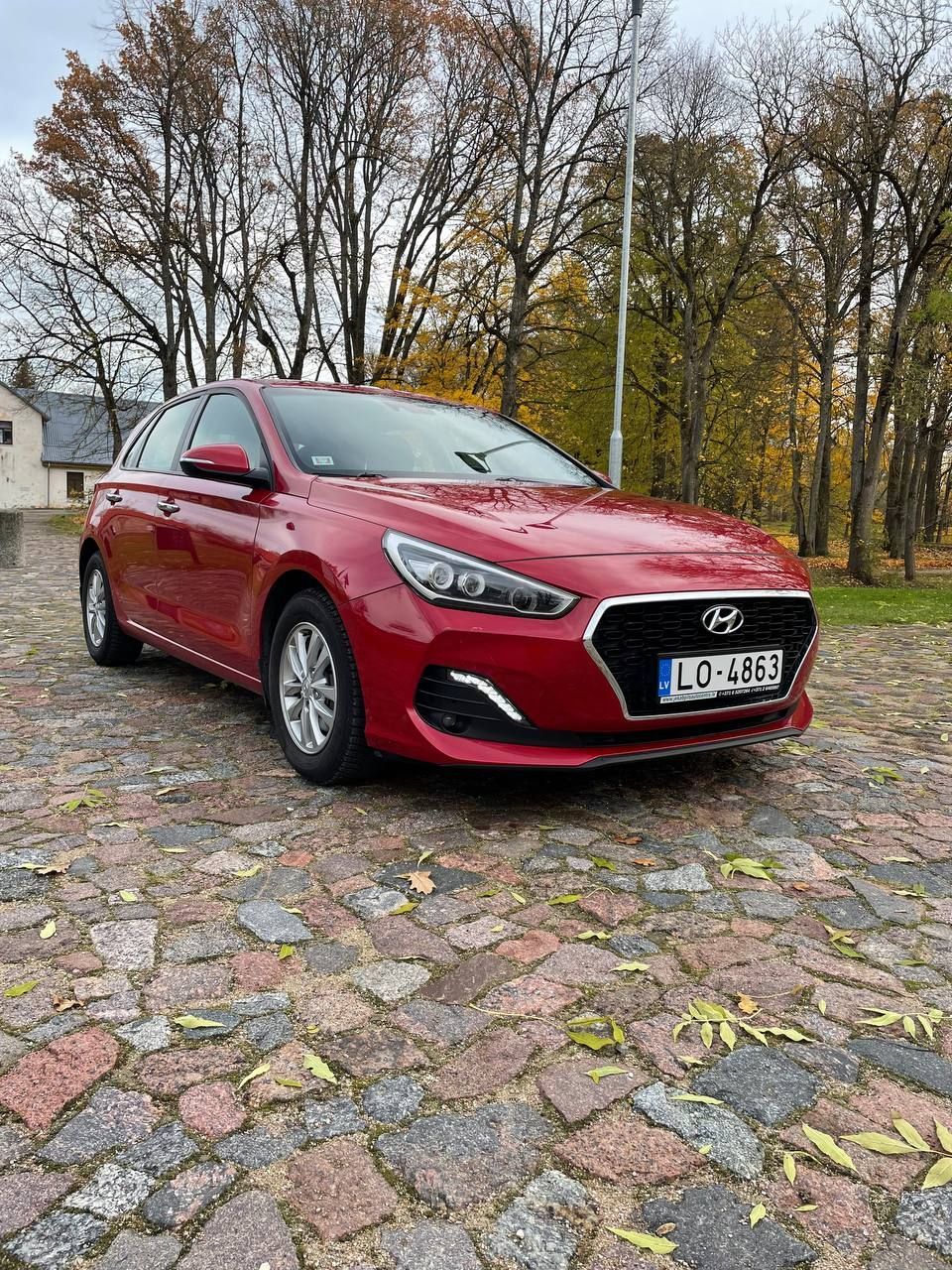 Sarkans hyundai i30 stāv uz bruģakmens ielas.