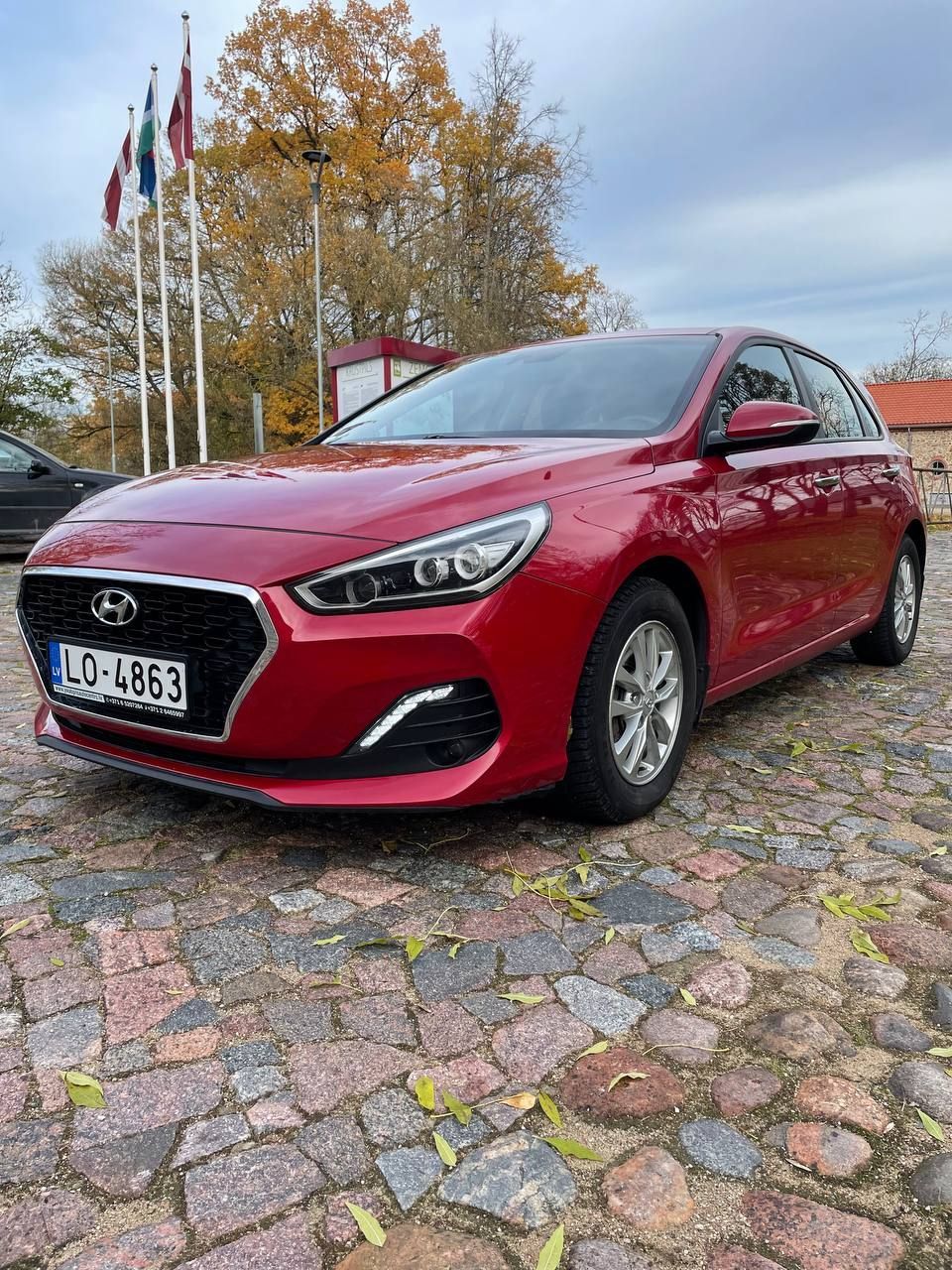 Sarkans hyundai i30 hečbeks ir novietots uz bruģakmens ielas.