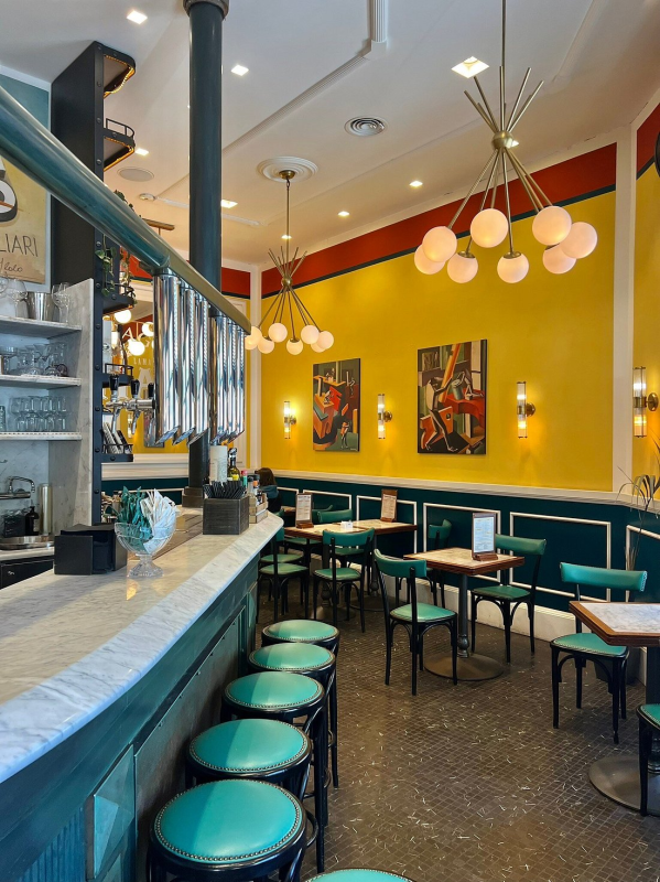 Interno di un bar con pareti gialle, finiture verde acqua e sgabelli rotondi verde acqua. 