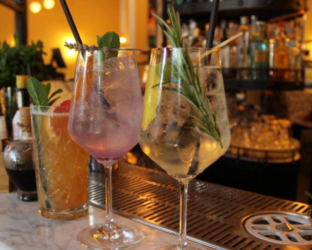 Tre cocktail con guarnizioni sul bancone: fetta d'arancia, menta e rosmarino.