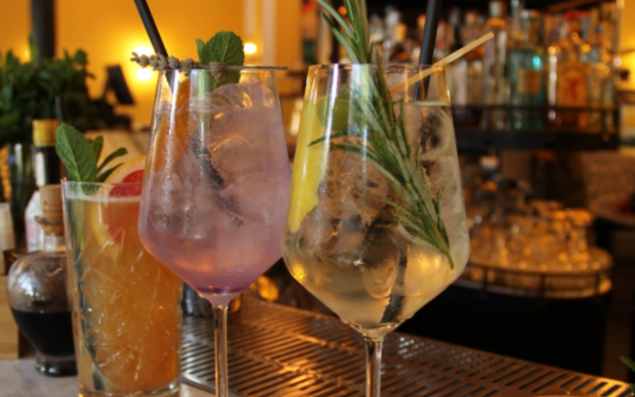 Tre cocktail con gambo e guarnizioni su un bancone; sullo sfondo è visibile un bancone.