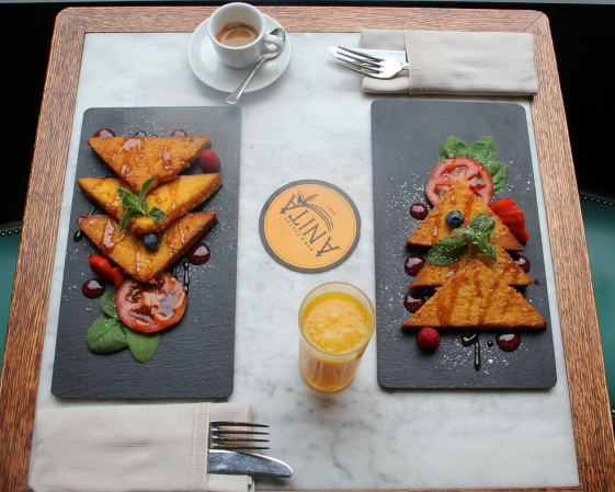 Due piatti di pane tostato alla francese, caffè espresso, succo di frutta e posate sono disposti su un tavolo.