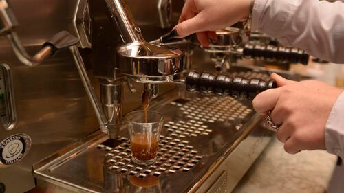 Preparazione dell'espresso con una macchina, liquido marrone versato in un bicchiere trasparente, 