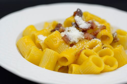 Pasta alla carbonara in una ciotola bianca, con pasta gialla, pancetta e formaggio grattugiato.
