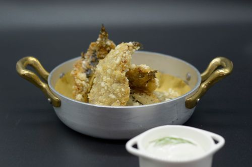 Cibo fritto in una piccola ciotola di metallo con manici dorati, servito con una piccola ciotola di besciamella.