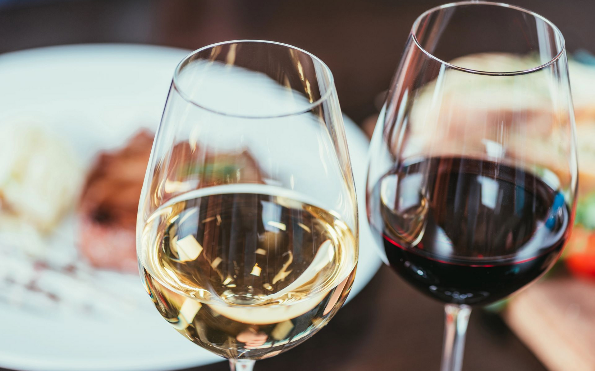 Due bicchieri di vino, uno bianco e uno rosso, davanti a un pasto sfocato.