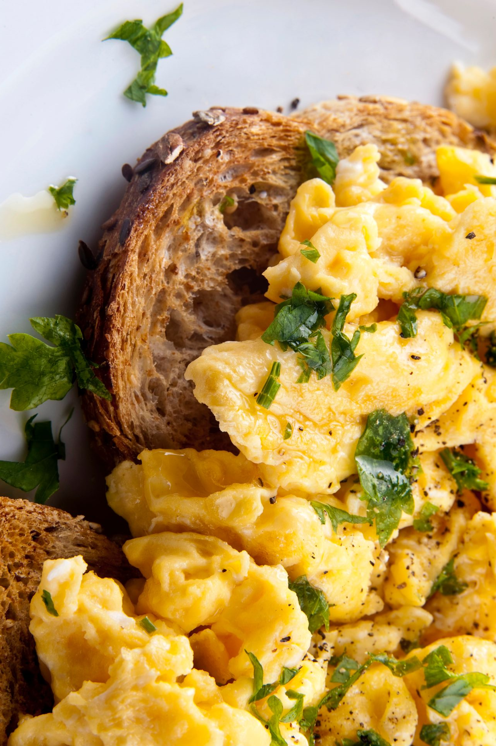 Uova strapazzate con erbe aromatiche tritate su pane tostato, primo piano.