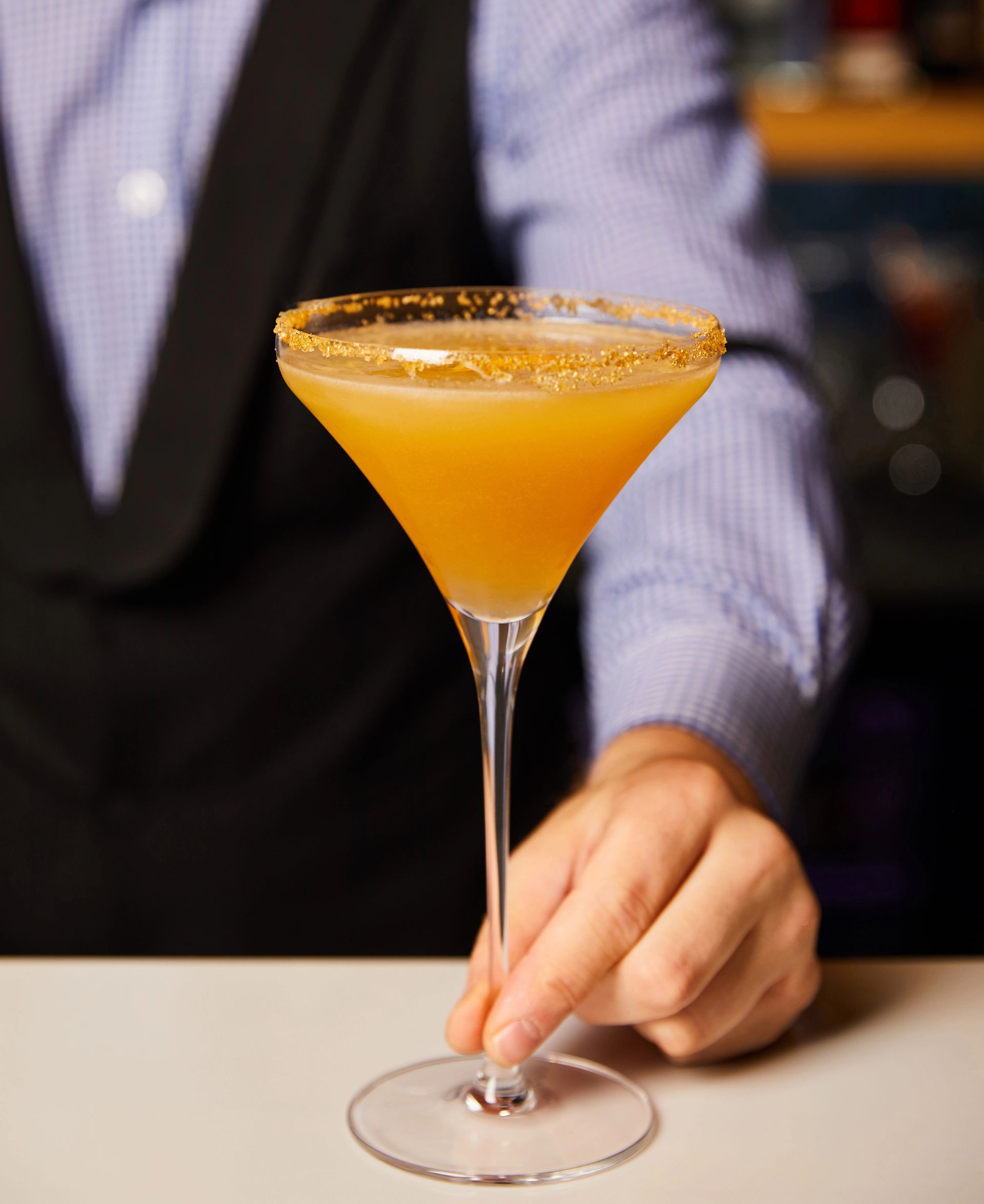 Barista che tiene in mano un cocktail in un bicchiere da martini, un drink all'arancia con il bordo zuccherato.