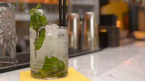 Cocktail Mojito con guarnizione di menta, ghiaccio e cannuccia sul bancone.