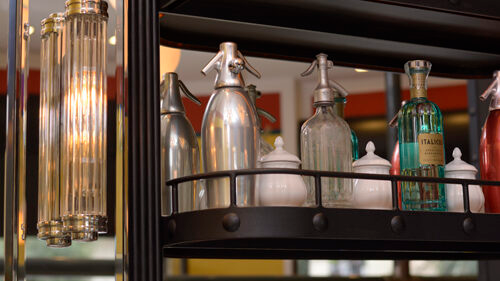 Mensole con sifoni e bottiglie di soda d'epoca, con una lampada decorativa sulla sinistra.