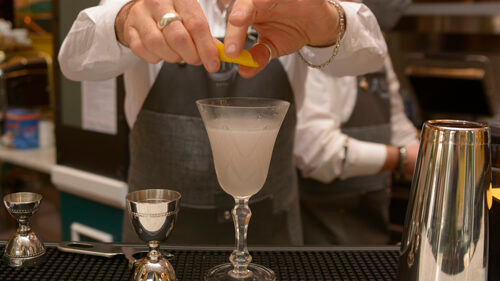 Barista che spreme la scorza di un agrume in un bicchiere da cocktail. Ambiente da bar.