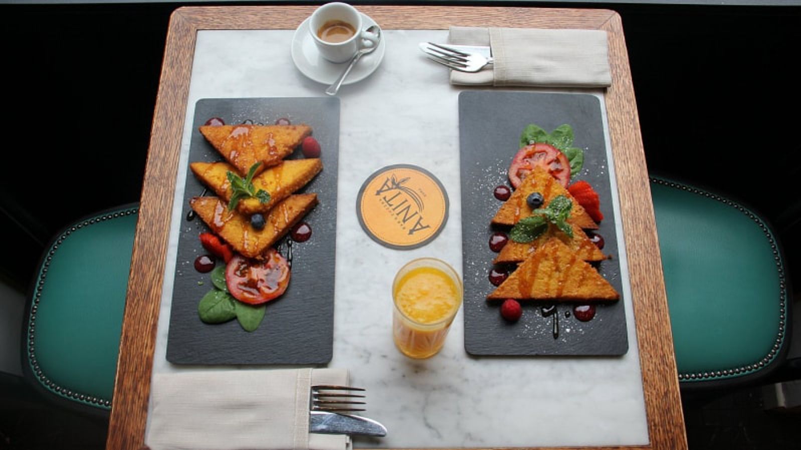 Due piatti di french toast con frutta, un caffè, succo di frutta e posate su un tavolo.