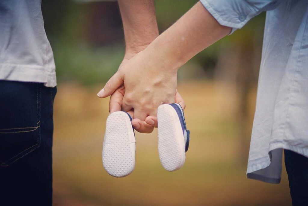 A man and a woman are holding hands and holding baby shoes.