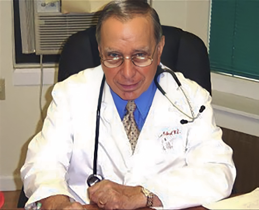 A doctor is sitting at a desk with a stethoscope around his neck