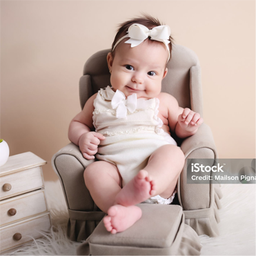 A baby girl is sitting in a chair with a bow on her head