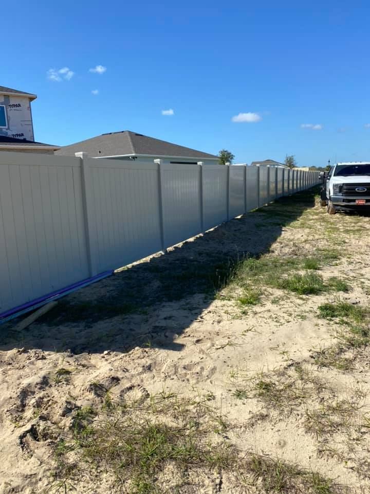 A white fence is sitting in the middle of a dirt field next to a house.