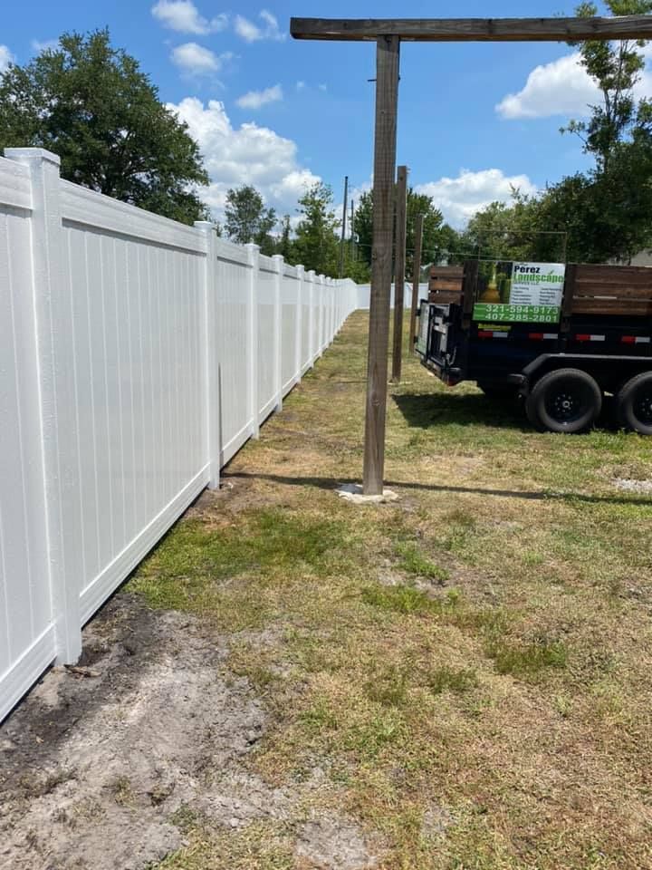A white fence surrounds a yard with a dumpster in the background.