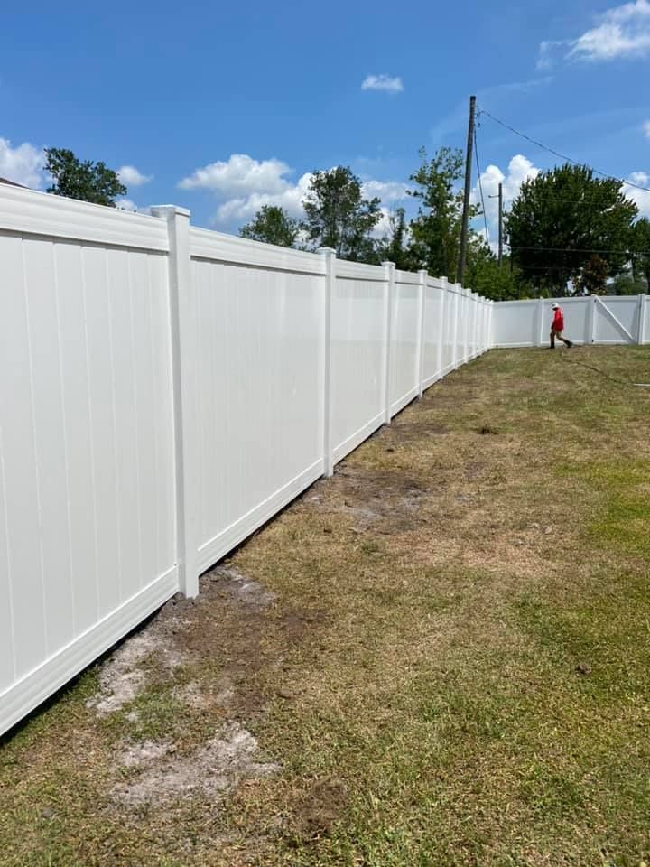 A white vinyl fence is sitting in the middle of a grassy field.