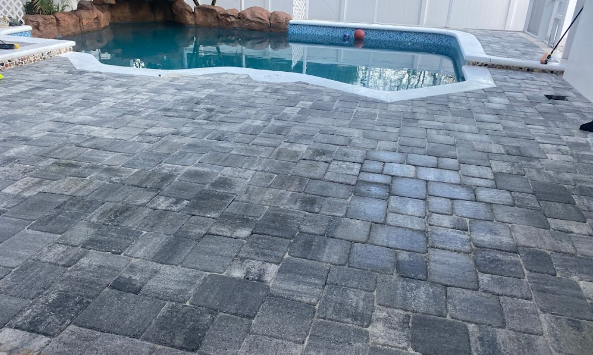 A swimming pool with a brick patio in front of it.