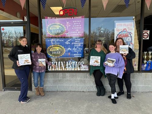 Five people stand in front of a shop window, holding books. Signage says 