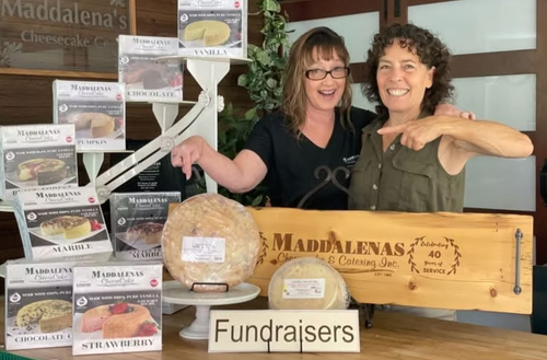 Two women are standing next to a wooden sign that says fundraisers.