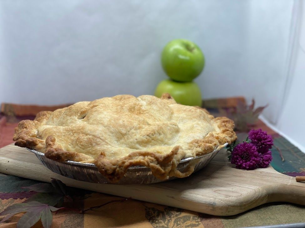 An apple pie is sitting on a wooden cutting board.