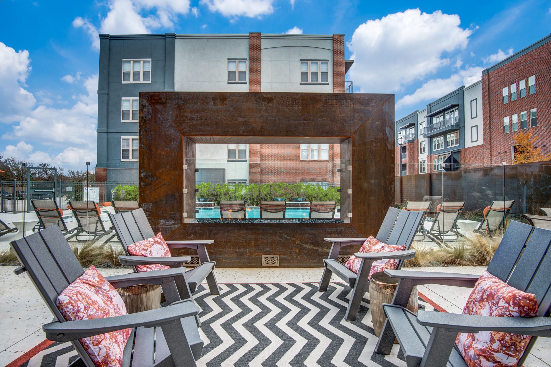 An outdoor patio area with chairs and a fireplace in front of apartment buildings at Two99 Monroe offers apartments for rent in Roanoke, TX.