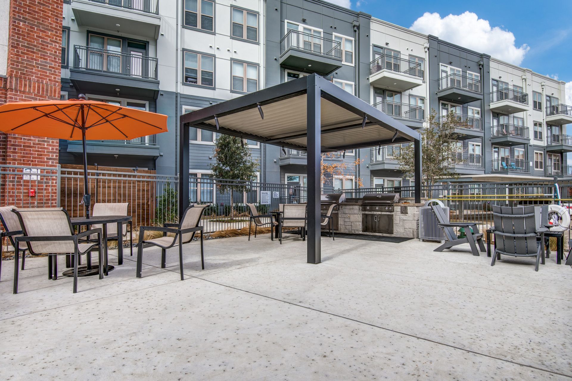 A patio area with tables and chairs and an umbrella in front of a building at Two99 Monroe offers apartments for rent in Roanoke, TX.